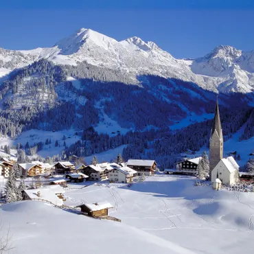 Online booking special Snow-covered Alpine village with church and mountain backdrop on a clear winter day
